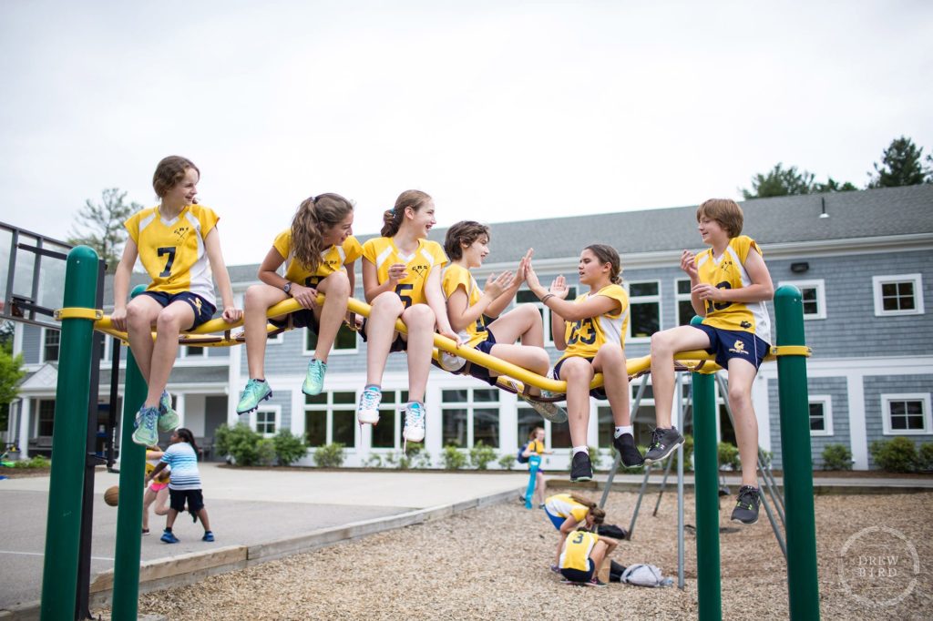 A group of girls in lacrosse uniforms sit on top of jungle gym on campus at the Charles River School in Boston. San Francisco education marketing photographer Drew Bird. San Jose school branding photographer.